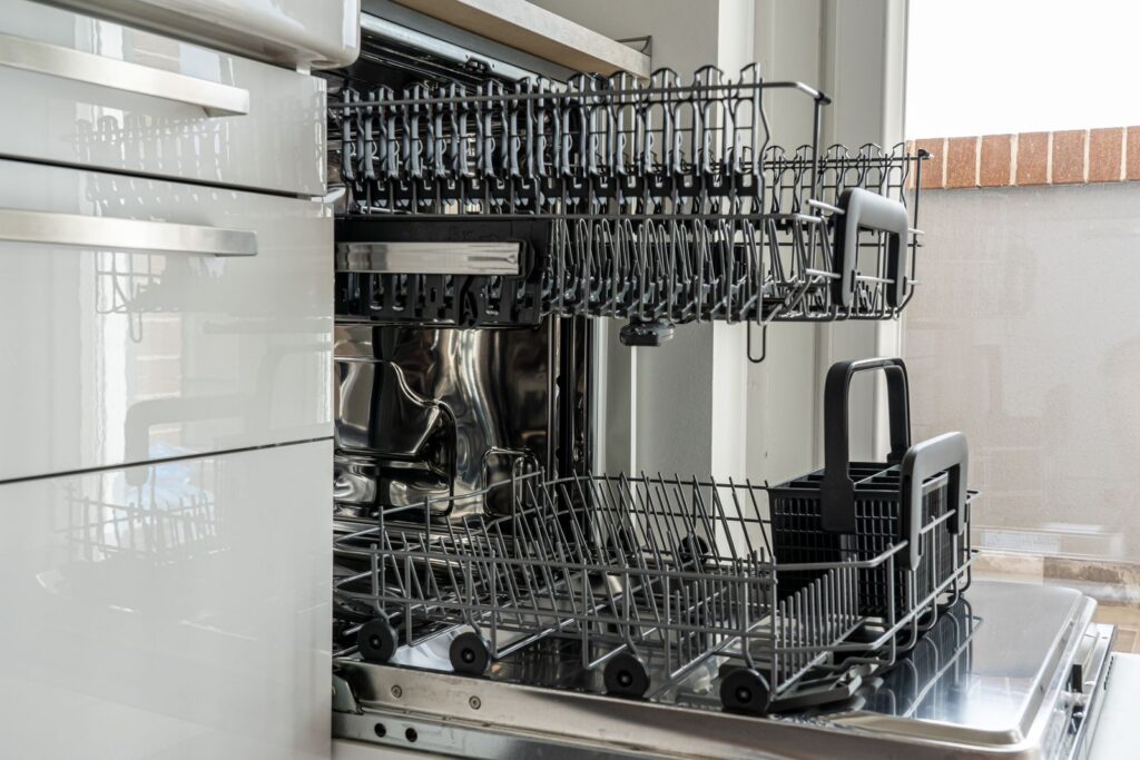 Lave-vaisselle ouvert dans une cuisine, paniers sortis avant nettoyage des bras de lavage